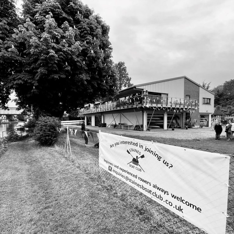 Modern Staines Boat Club Surrey Black and white photo of a building with a banner outside, surrounded by greenery.