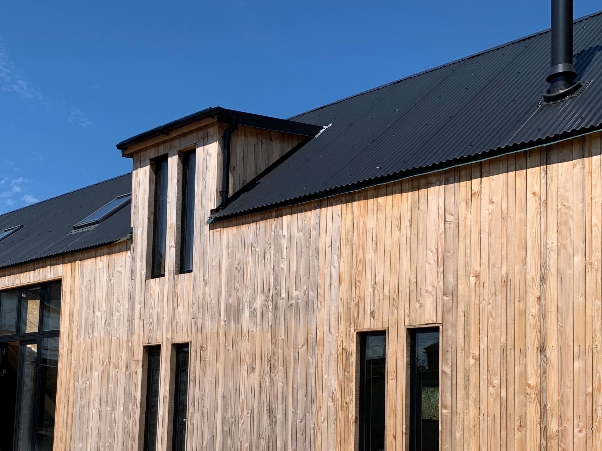 Walnut Barn, Stoney Stratton Modern wooden-clad building with large windows and a peaked roof against a blue sky.